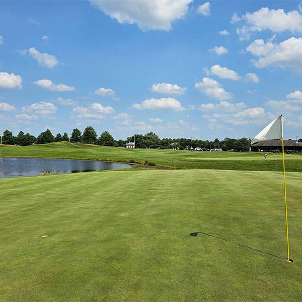 Lederach Golf Club course view from the green with a white flagstick in the hole and water obstacle in the background.